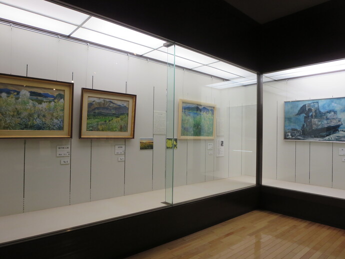 ガラス張りの大きな展示ケースの中に、豊かな自然風景や山々を描いた数枚の油彩画がゆったりと間隔を空けて掲示され、それぞれの作品の下には解説プレートが添えられている展示風景の写真