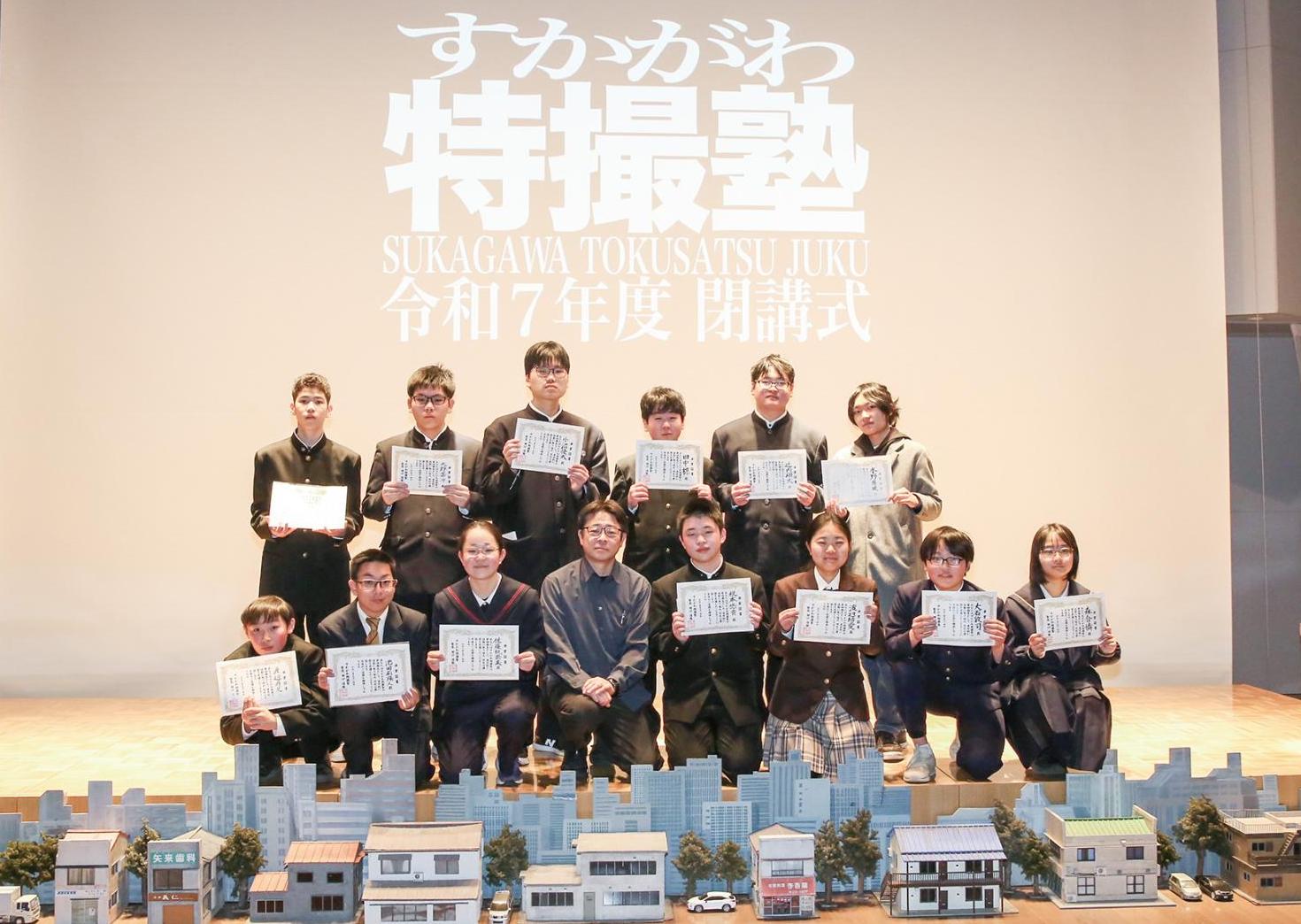 街の特撮セットと一緒に、塾生の子どもたちと講師の男性が並んだ集合写真