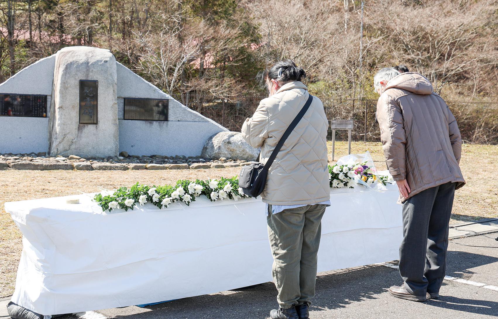 慰霊碑の前にある献花台で男性と女性が追悼している風景