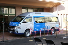 シルバーとブルーの車体に「ちょこすか 01」というロゴが描かれたコミュニティバスの周りに、開通を祝う紅白のテープが張り巡らされている写真