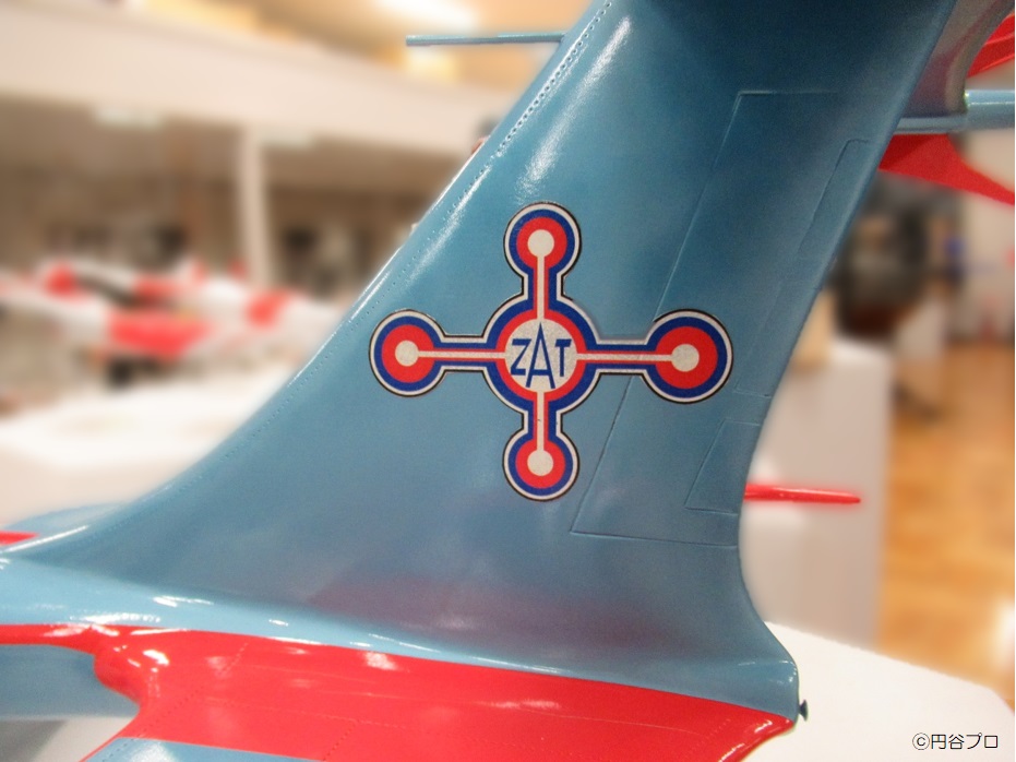 水色の機体に赤と白のラインで構成された「ZAT」の文字入り十字マークが描かれた、特撮作品に登場する「スカイホエール」の模型の垂直尾翼部分を捉えた写真