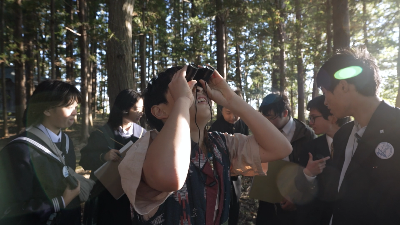 不思議な童と野鳥部の学生たちが出会い、童が双眼鏡の性能に驚いている様子