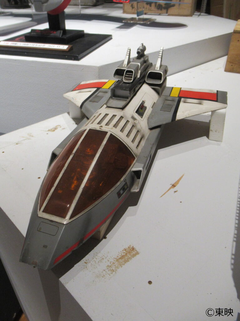 機首がグレーで翼に赤と黄色のラインが入った古い戦闘機の模型が展示台に置かれた写真