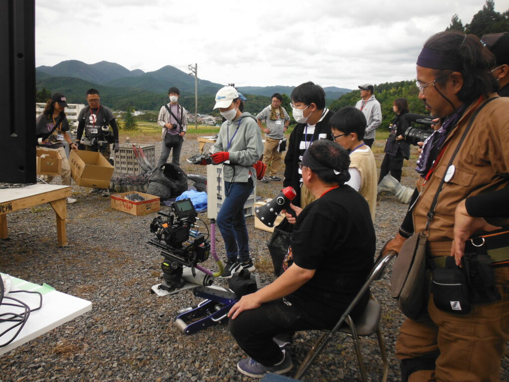 ビデオカメラが置かれ、撮影した映像を確認しているスタッフと塾生の写真