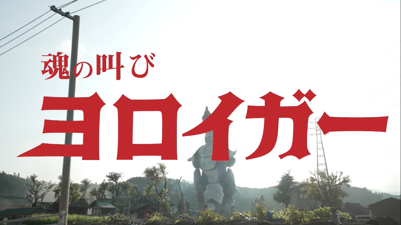 屋外に立つ巨大な怪獣のシルエットを背景に、赤色で大きく「ヨロイガー」という番組ロゴと、その上に小さく「魂の叫び」という文字が重ねられた、特撮作品のワンシーンのような迫力ある実写写真