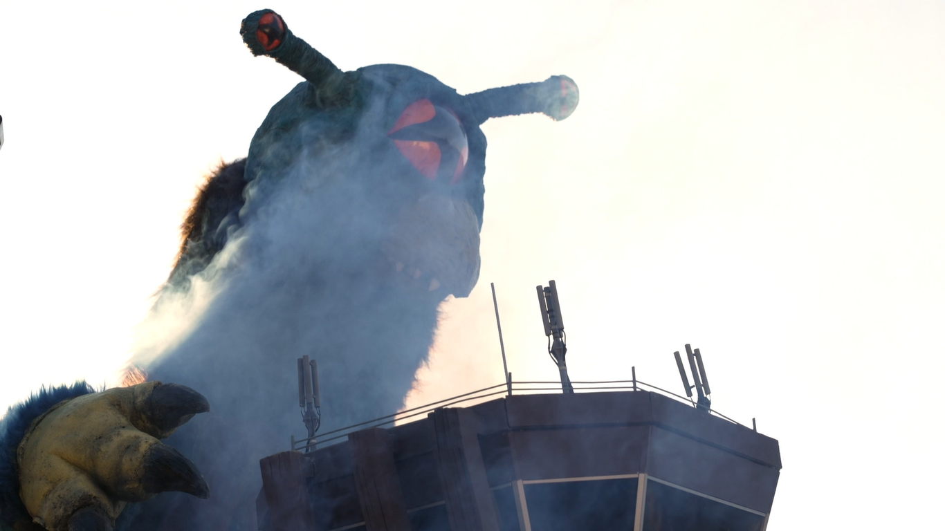 怪獣フェザーロンが空港の管制塔の上部を抱きかかえるほど近くにいる様子の首から上部分のアップ