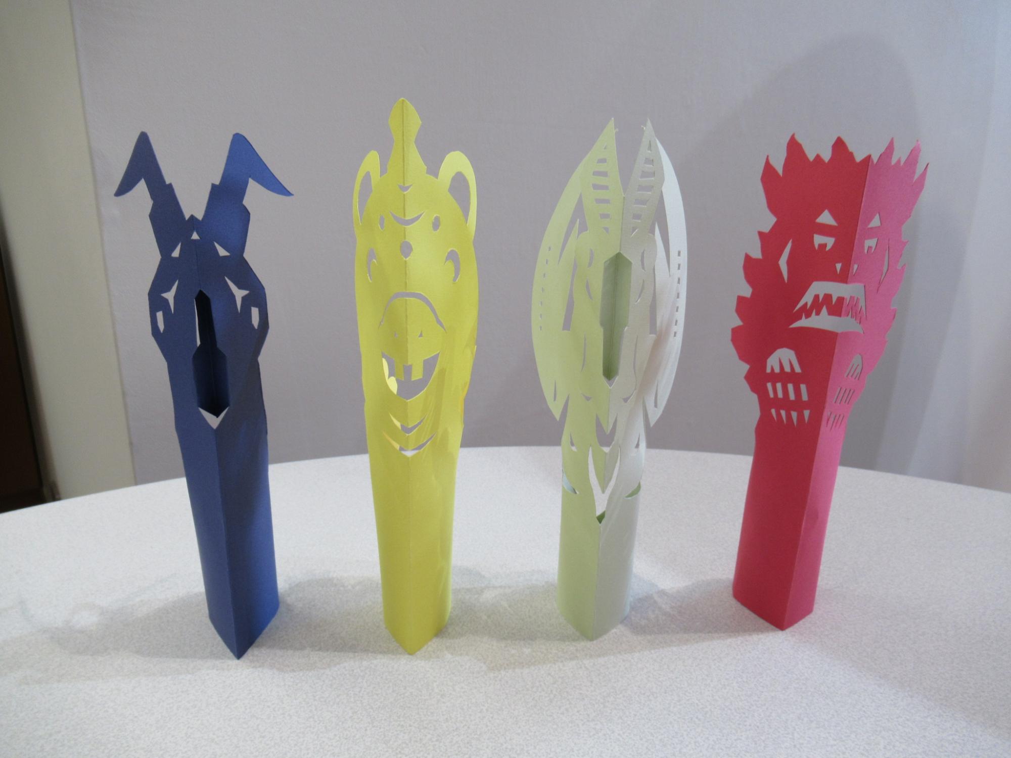 淡い色合いと濃色の紙で精巧に切り抜かれた四体の立体的な怪獣の造形作品が卓上に整然と並ぶ様子の写真