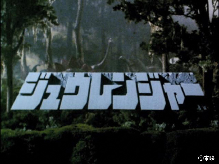 鬱そうと茂る暗い森を背景にして、画面中央に石のような質感で「ジュウレンジャー」という力強いフォントのタイトルロゴが大きく配置され、その背後の木々の間には首の長い恐竜などのシルエットがうっすらと見える特撮番組のタイトル画像写真