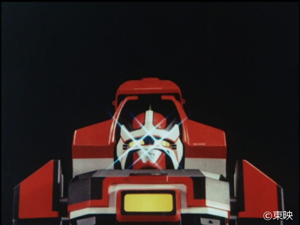 漆黒の闇の中から、赤と白の鮮やかなカラーリングが施された巨大ロボットの頭部が、両目を鋭く光り輝かせながら迫り出してくる静止画写真