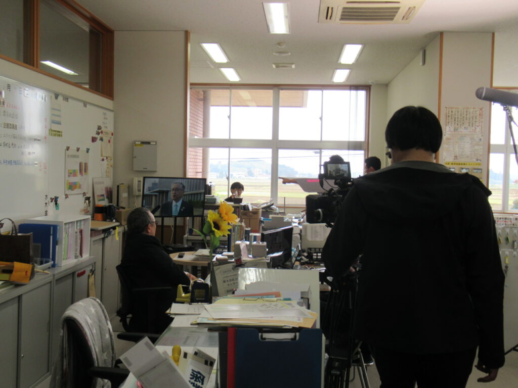 室内で、モニターに映る人物の映像を確認しながら、カメラマンやスタッフが機材を構えている様子の写真