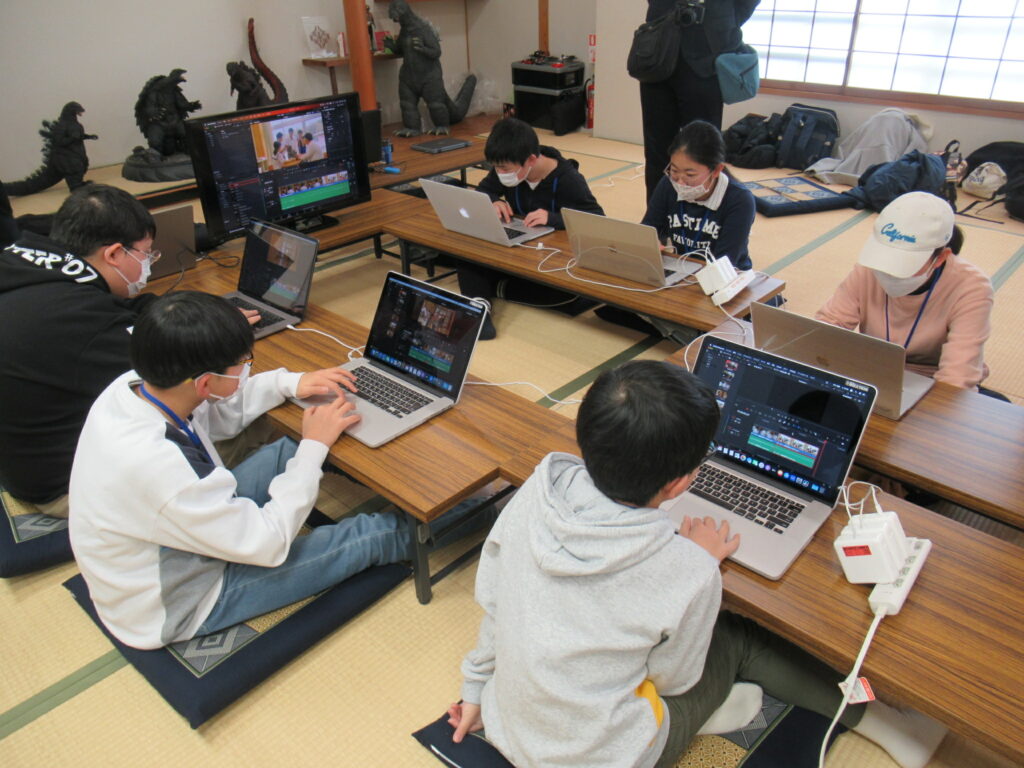 和室に並べられた長机を囲み、複数の参加者たちがノートパソコンを操作しながら、モニターに映る編集画面を見つめて作業に取り組んでいる写真