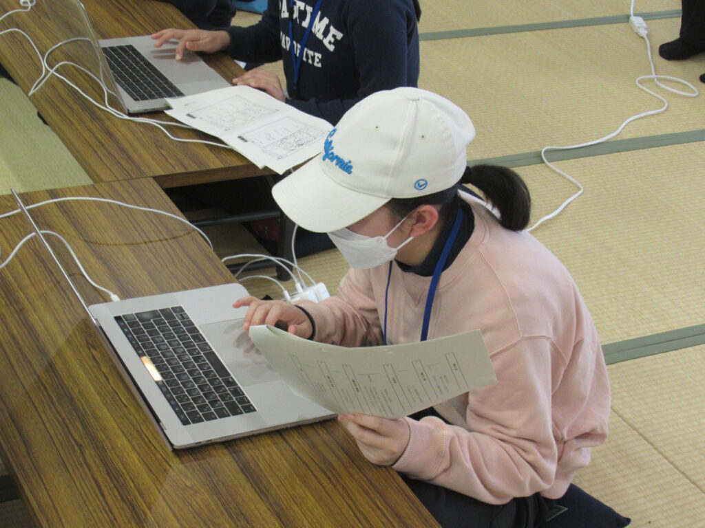 和室の長机でノートパソコンに向かう参加者が、片手に資料を持ちながら画面を真剣に操作している様子の写真