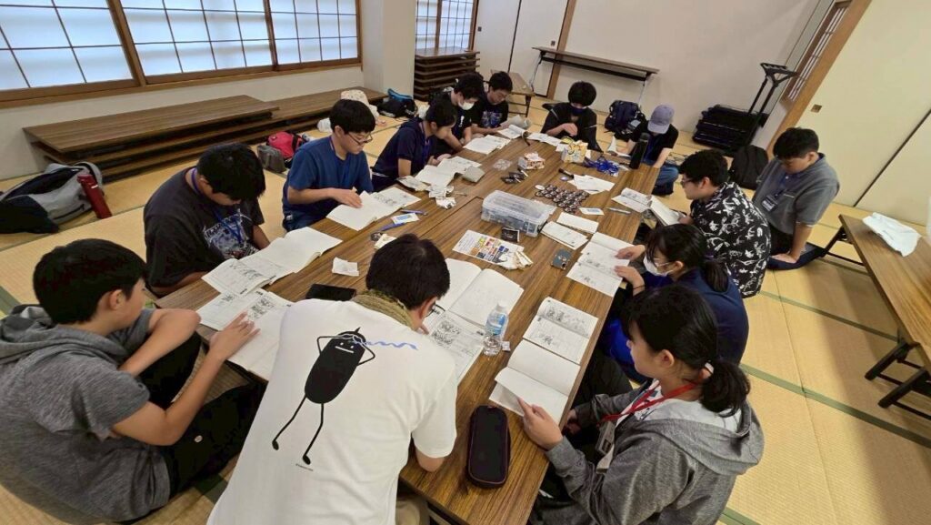 長机を囲んだ参加者たちが資料やノートを広げ各自のページを読み進めながら熱心に学ぶ様子の写真