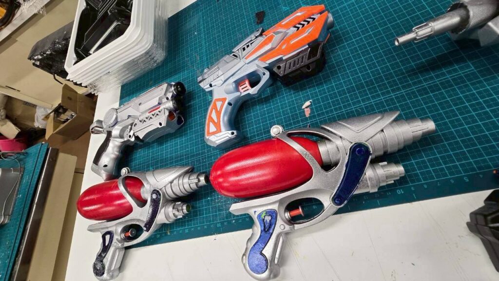 銀色と赤の装飾が施された玩具銃が作業台のカッターマット上に整然と並べられている様子の写真