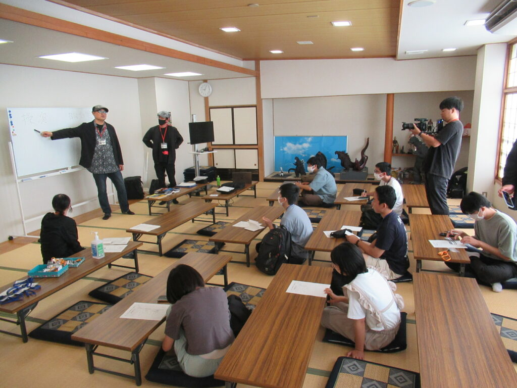 畳の部屋で講師がホワイトボードを指し示し、低い机に座った参加者が資料や筆記用具を前に熱心に学ぶ様子を広く捉えた写真