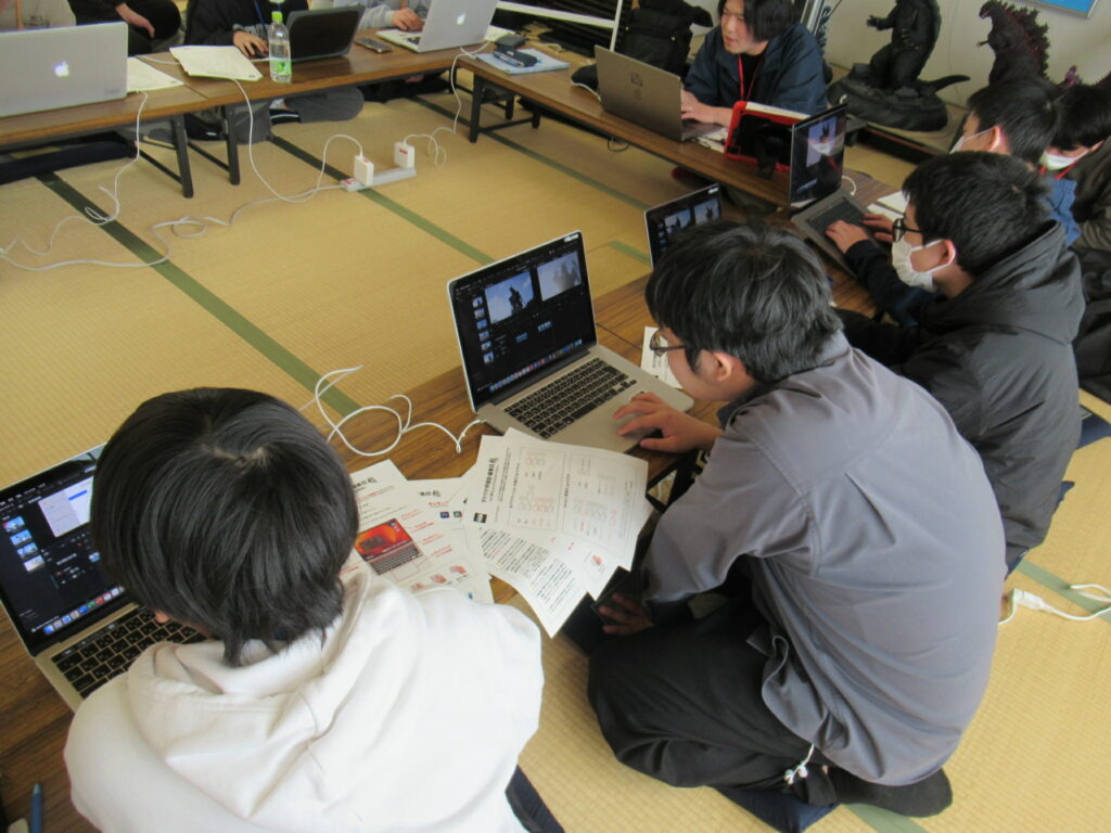 畳敷きの和室で、長机に向かった学生たちが各自のノートパソコンを広げ、配布された資料を確認しながら動画編集ソフトを操作して特撮映像の制作や加工に取り組んでいる写真