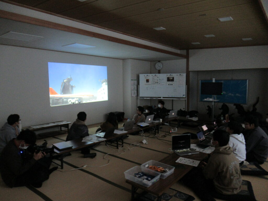 薄暗い畳の部屋で参加者たちがノートPCを前に大型スクリーンの映像を静かに鑑賞する様子の写真
