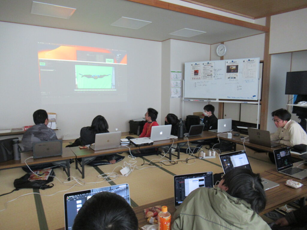 畳の部屋で参加者たちがノートPCを広げ大型スクリーンに映る映像編集画面を真剣に見つめる写真