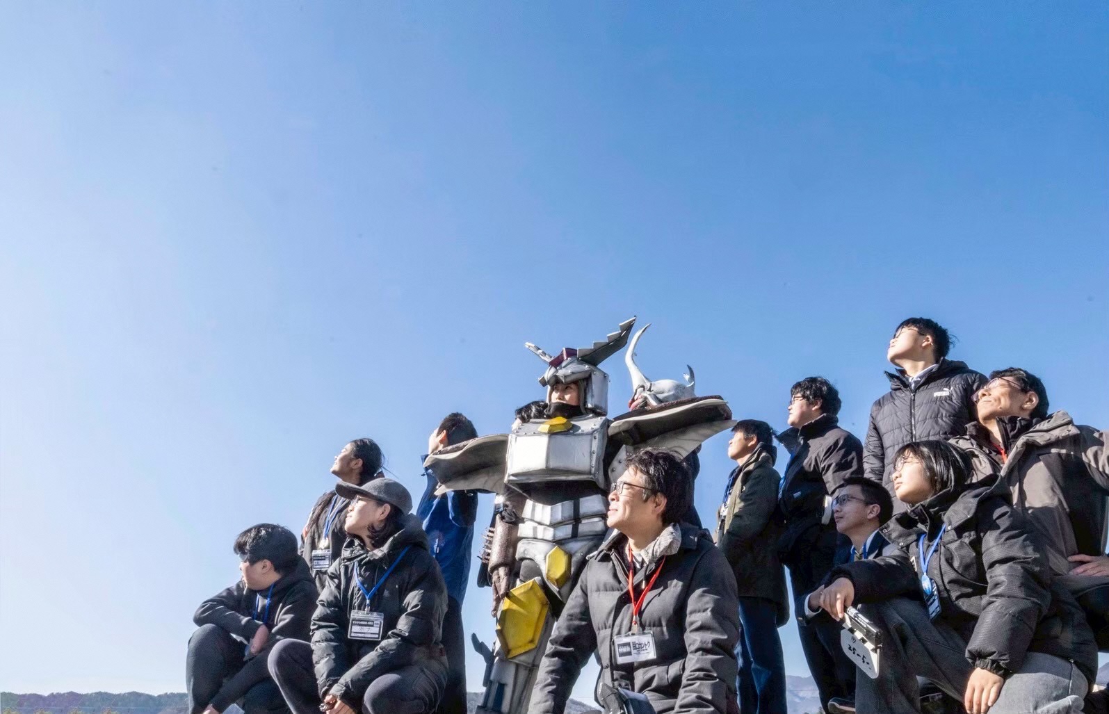 すかがわ特撮塾の塾生と講師陣が青空をバックに空を見上げたポーズをとっている集合写真