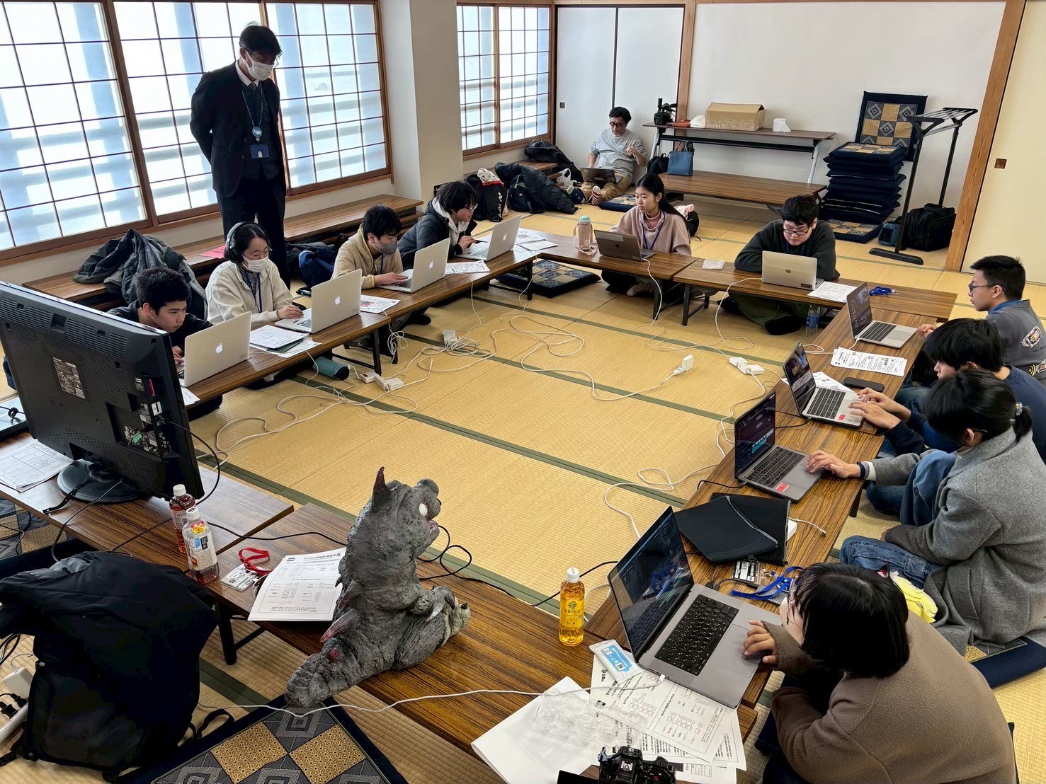 和室にロの字の形で机が並べられており、それぞれノートパソコンで映像編集作業をする塾生が席についている様子