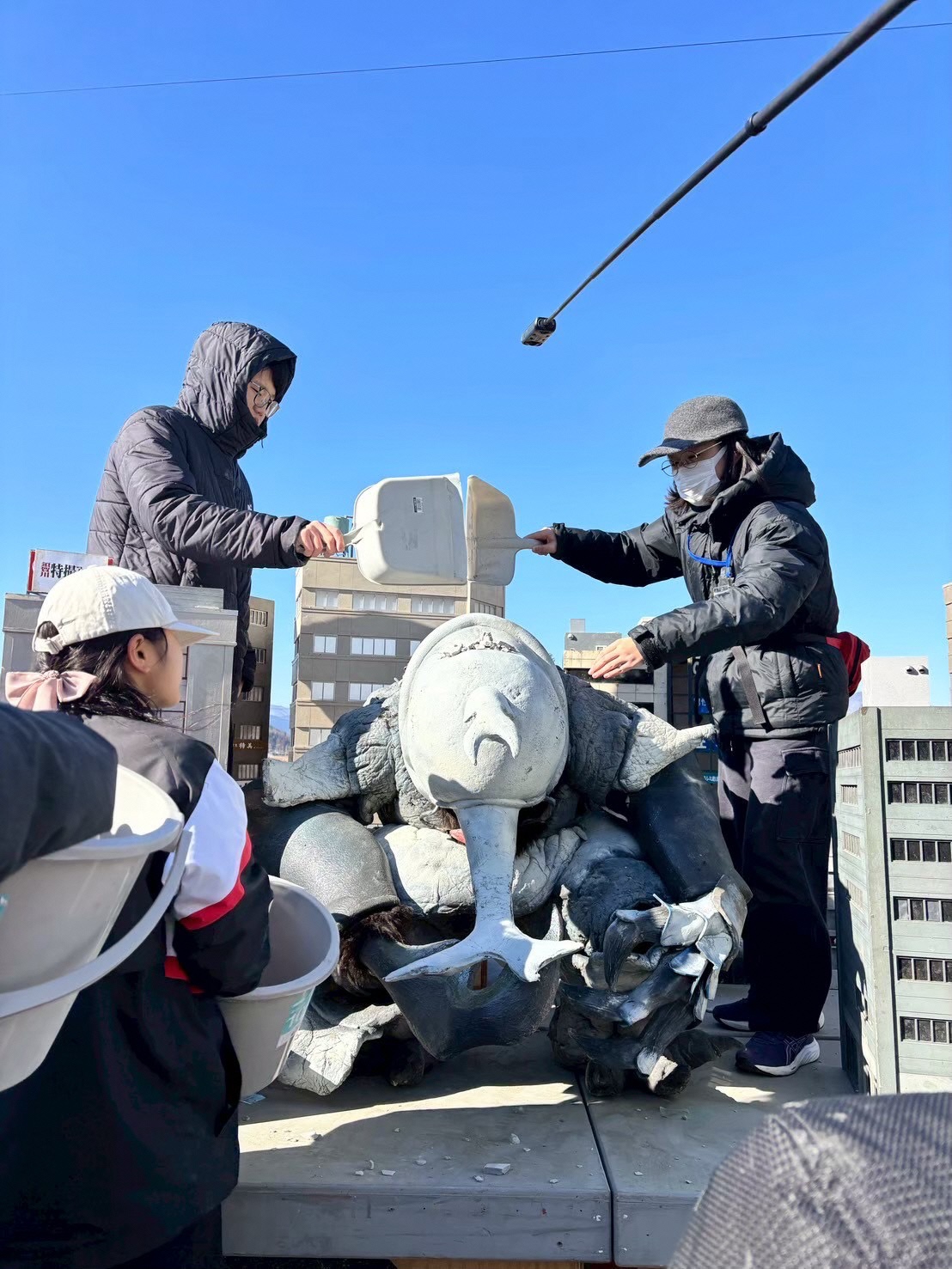 屋外での特撮カットの撮影準備をしている様子、怪獣が起き上がるシーンを効果的に見せるためにかがんだ状態の怪獣に石膏ガラと呼ばれる細かく砕いた石膏を載せている