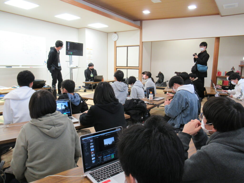 畳敷きの和室で多くの塾生が低い長机に向かって座り、前方のホワイトボードやモニターを見つめながら講師の説明を熱心に聞いたりメモを取ったりしている写真