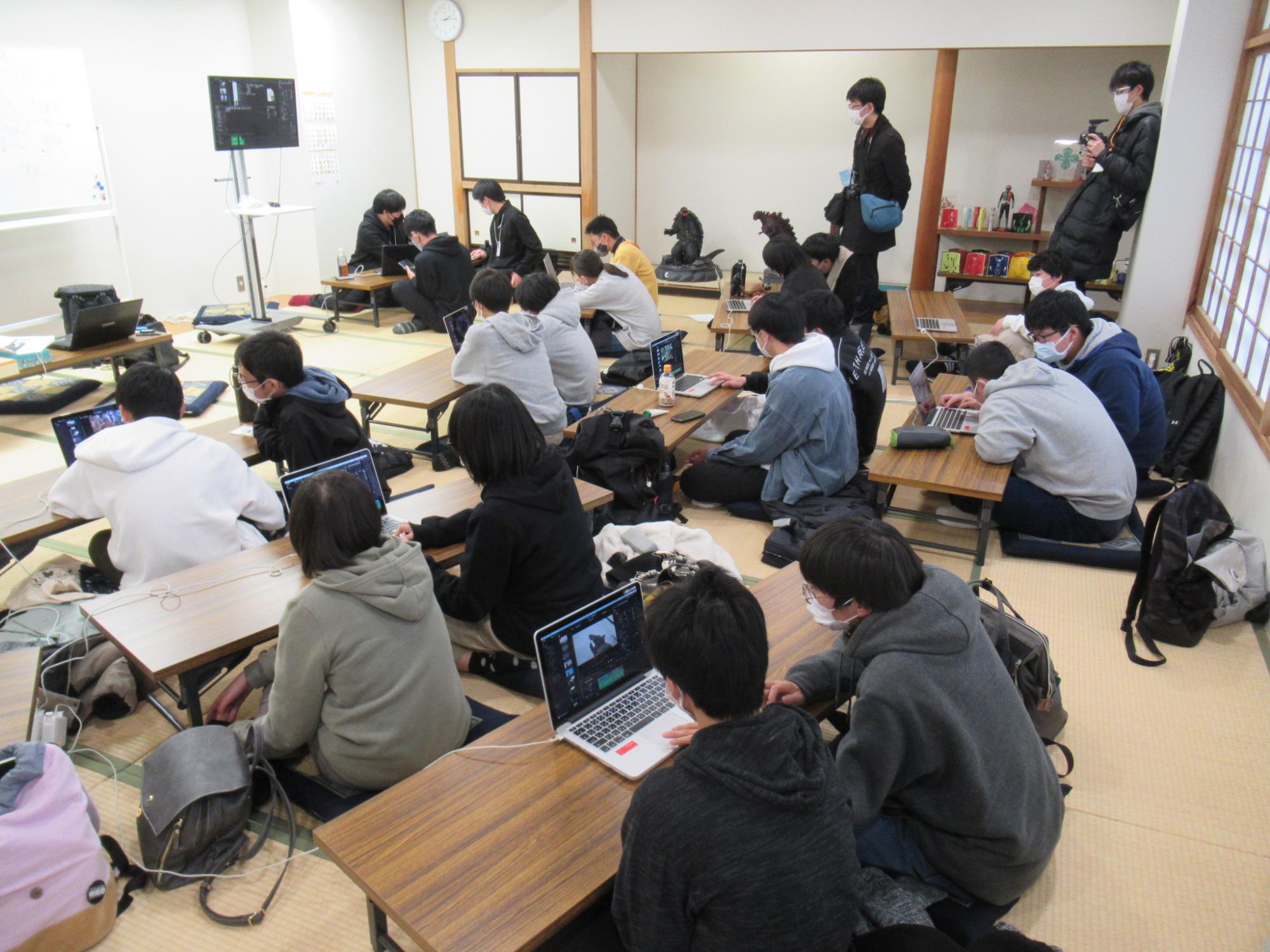 畳敷きの和室で、多くの塾生が低い長机に向かって座り、ノートパソコンを操作しながら画像を見ている写真