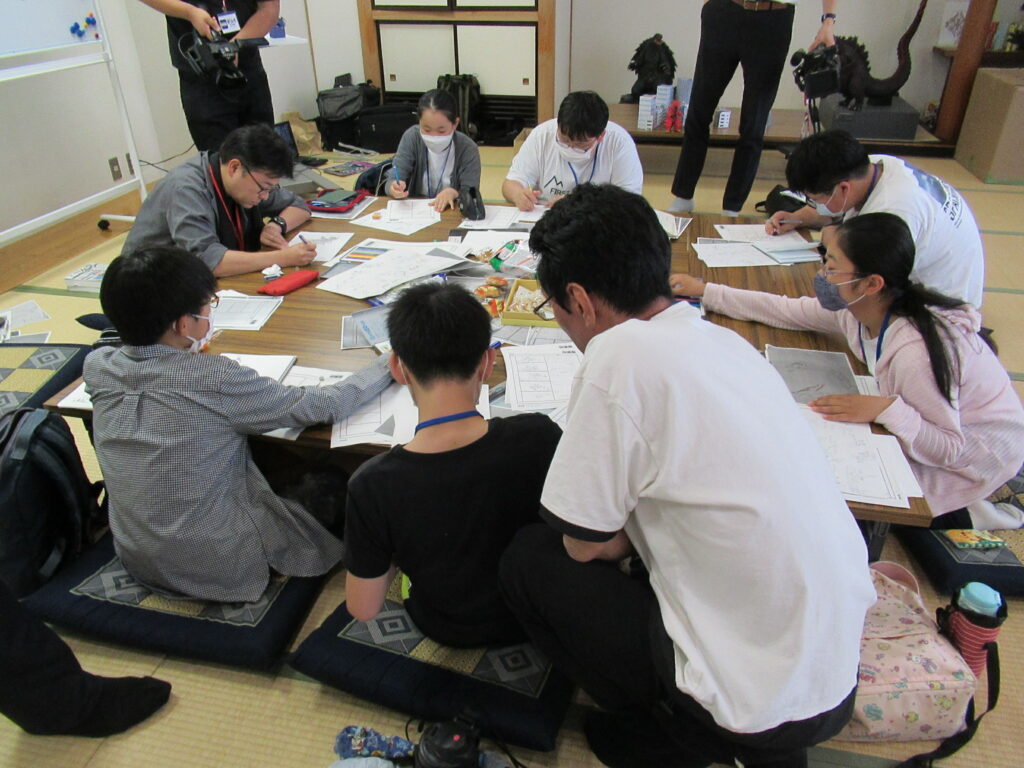 木目調の机を囲み塾生たちが資料に書き込みをする中、塾生の隣でフォローに入る講師の写真