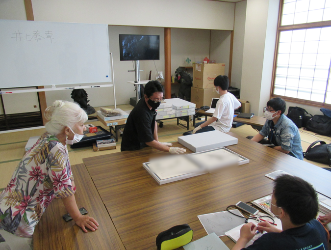 木目調の机をくっつけて大きなテーブルとした状態で、貴重な資料を広げている講師の様子の写真