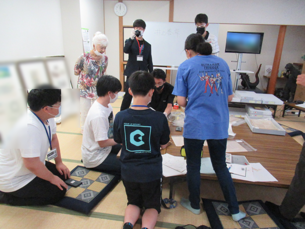 机の上の資料を見るために、座席を移動し講師の元に集まっている塾生たちとそれをカメラにとるスタッフの写真