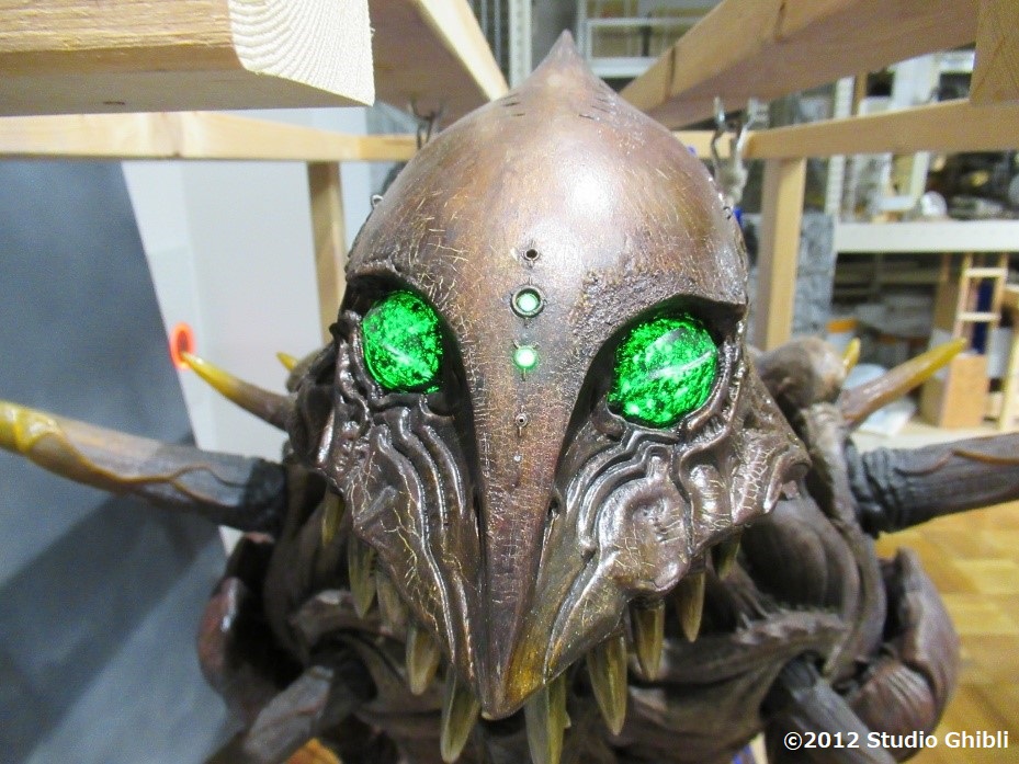 緑色の目に細かい傷や皺が刻み込まれた茶色い表面に覆われたFRP（繊維強化プラスチック）製のロッドパペットの頭部の写真