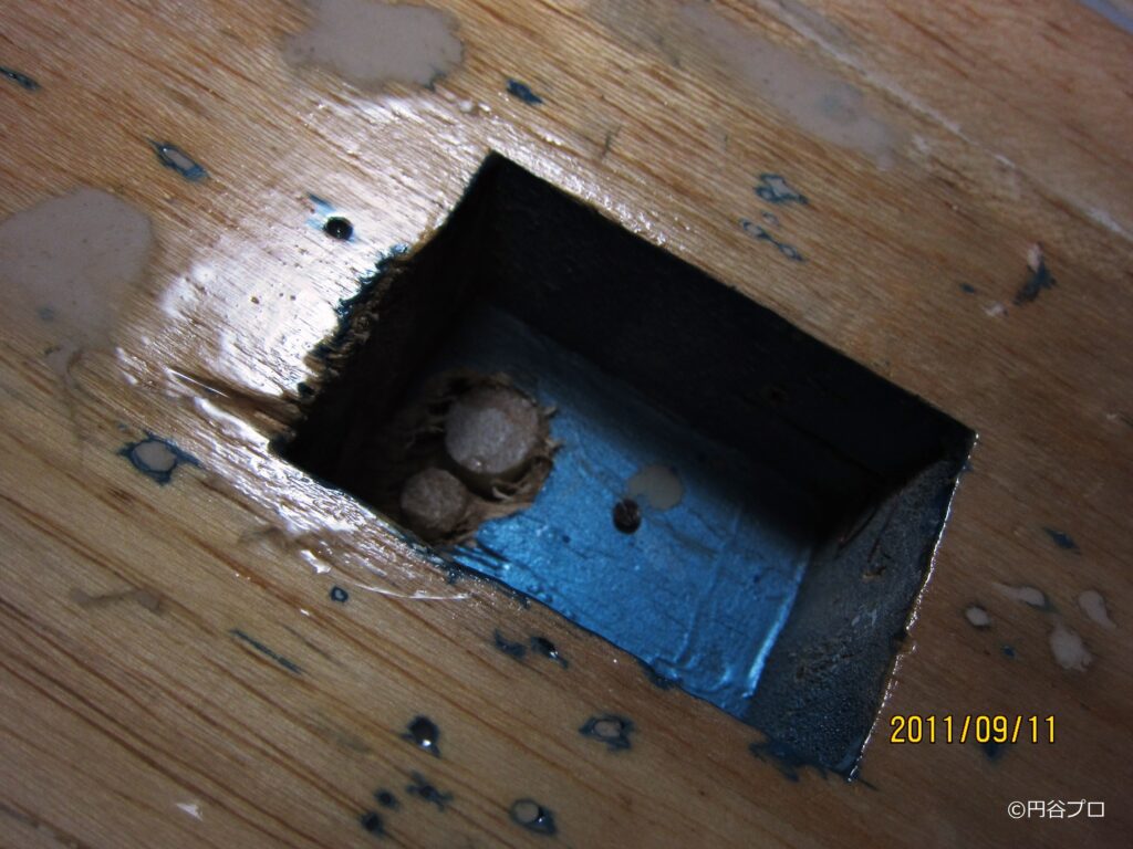 木目が見える大型戦闘機模型の表面に四角い穴が切り抜かれており、その内部に青い塗装と円柱状のパーツが覗いている様子を至近距離から撮影した写真