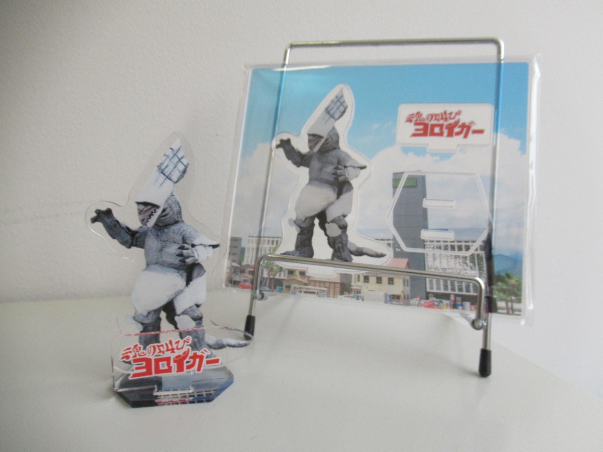 ヨロイガーが印刷されたアクリルスタンドの写真、左側には組み立てたもの、右側には組み立て前のものが並べられている