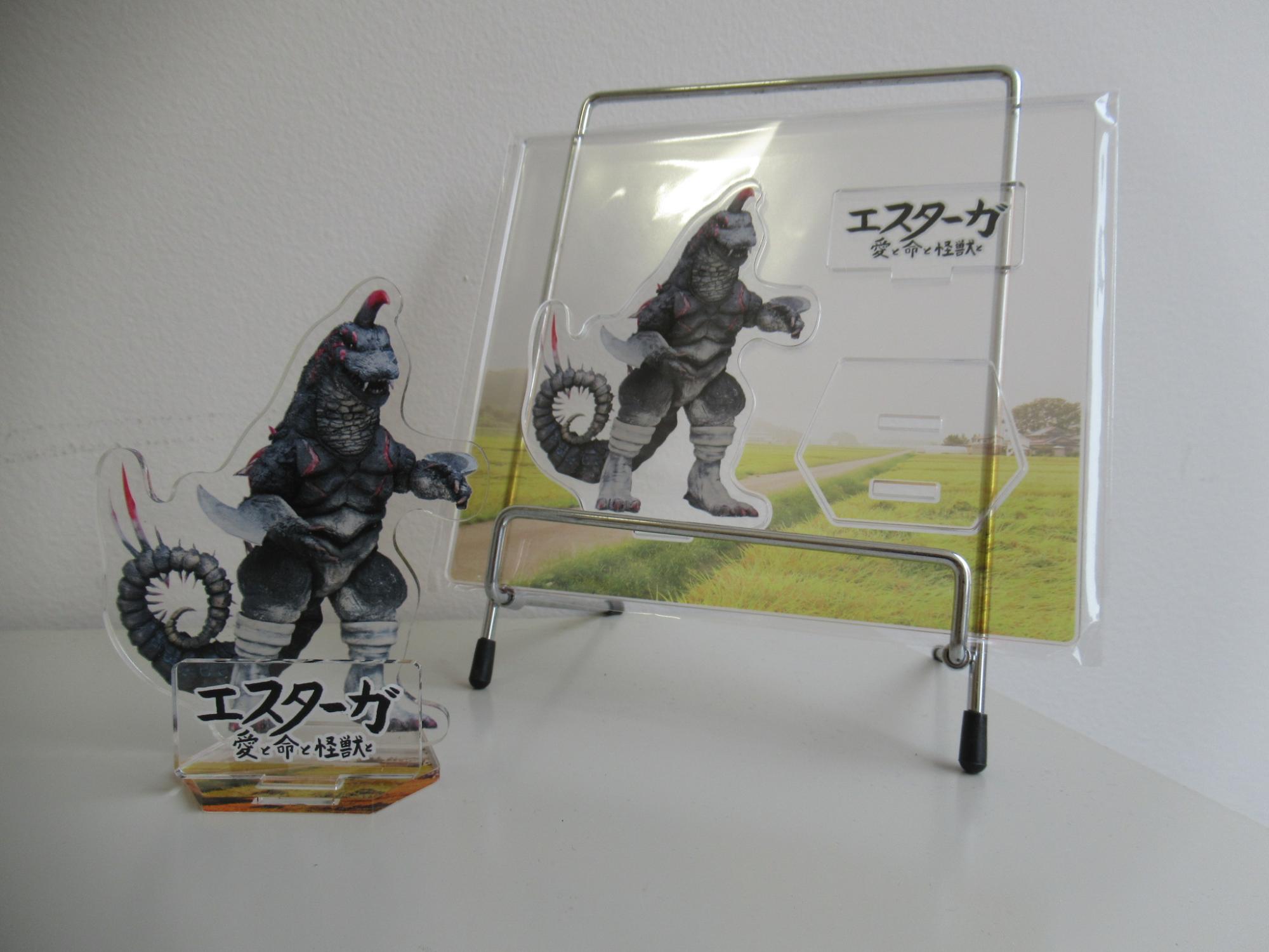エスターガが印刷されたアクリルスタンドの写真、左側には組み立て済みのアクリルスタンドが、右側には組み立てる前のプレートの状態のアクリルスタンドが並んでいる