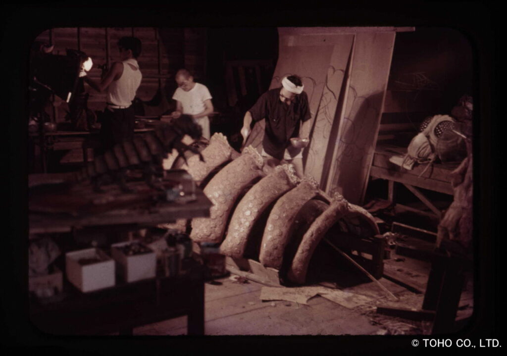 頭に鉢巻を巻いたスタッフたちが巨大なメガヌロンの着ぐるみの胴体パーツを制作している当時の古い写真