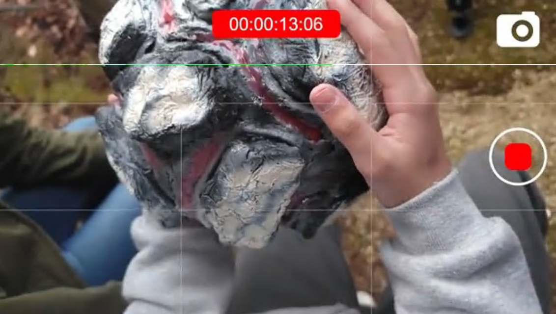 カメラ画面越しに人物が灰色と赤の隆起模様を持つ岩状の小道具を両手に持っている様子の写真