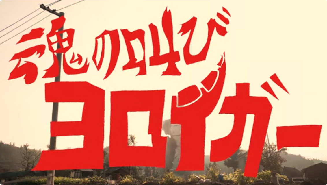夕景の屋外風景を背景に、力強く崩した赤い筆文字で「魂の叫びヨロイガー」と大きく重ねて配置し、情熱的で特撮作品の世界観を強く印象付けるタイトルロゴ画像