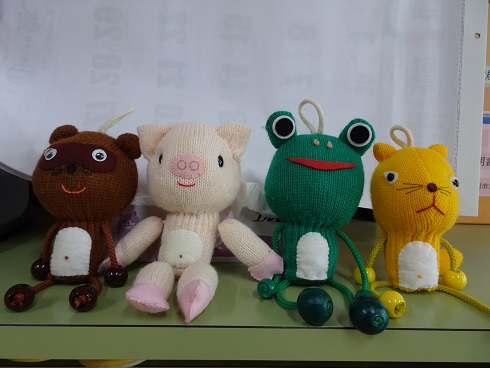 棚の上に左から茶色のクマ、淡いピンクのブタ、緑のカエル、黄色のネコが配置されて4体のぬいぐるみが並んで置かれている写真