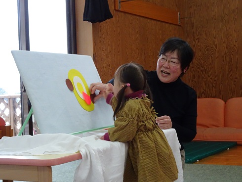 茶色の服を着た子どもがパネルシアターで遊んでいる様子の写真