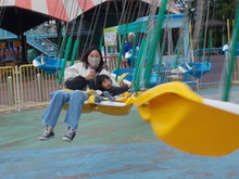 遊園地で黄色い座席のチェーンタワーに親子二人が乗って楽しんでいる写真