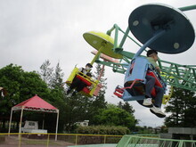 遊園地で、パラトルーパーに青と黄色の座席があり二人が乗って宙に浮いて楽しんでいる写真