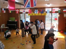 複数の大人と子どもが床に散らばったカラフルな玉を使って玉入れに挑戦している様子が写された写真