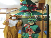 トナカイの着ぐるみを着た人物と、クリスマスツリーの帽子をかぶった人物、キャンディケーンを持つ緑の衣装の人物が並んでいる写真