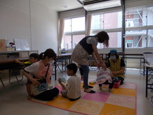 マットが敷かれた床に座り職員らが子どもたちに水分補給を行っている様子の写真