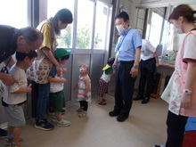 施設内で、数人の幼い子どもたちが職員と、校長先生に挨拶をしている様子の写真