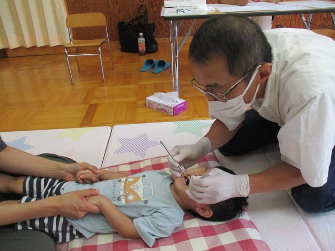 仰向けになった青い服を着た子どもが泣きながら、歯科検診を受けている写真