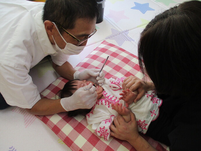 赤い模様入りの服を着た乳児が歯科検診を受けている様子を写した写真