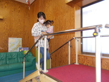 室内で、赤いカーペットが敷かれた小さな階段と手すりの上に、母親が幼児を抱いて立っている様子が写された写真