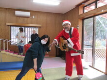 赤いサンタクロース衣装を着た人物がギターを持ち、隣で別の人物が手を合わせてポーズを取っている様子が写された写真