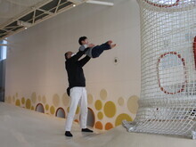 広い屋内の遊び場で、男性が幼児を両手で頭上に高く持ち上げ、遊具のネットの近くで遊んでいる様子の写真